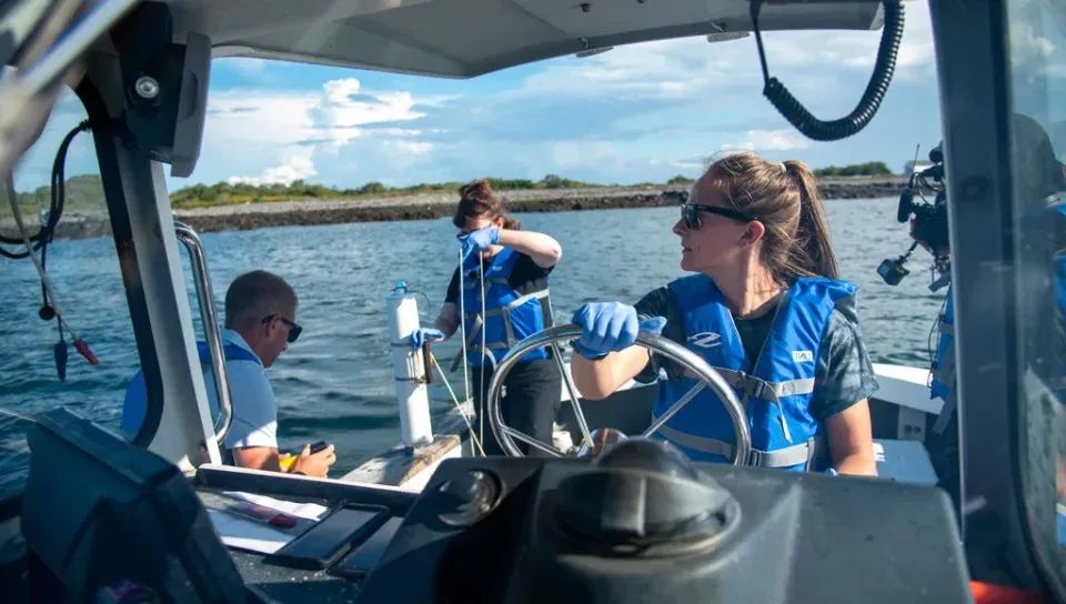 A U N E student wearing a blue life vest drives a boat in the ocean